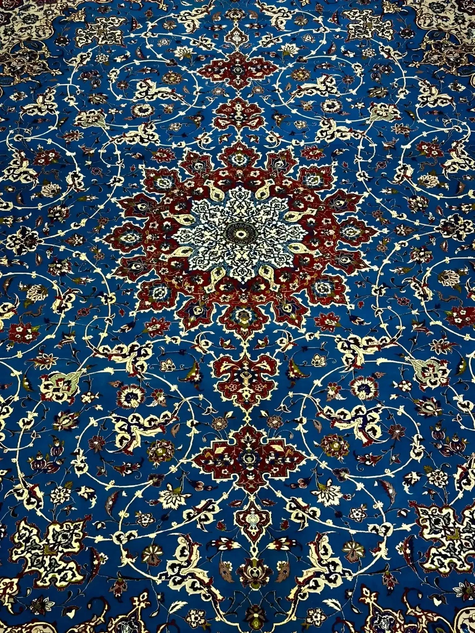 Elegant Floral and Geometric Patterns on Blue Persian Rug – A detailed image capturing the vibrant floral and geometric patterns across the blue field of a Persian rug, bordered by sophisticated accents of red, ivory, and gold, blending traditional artistry with luxurious elegance.